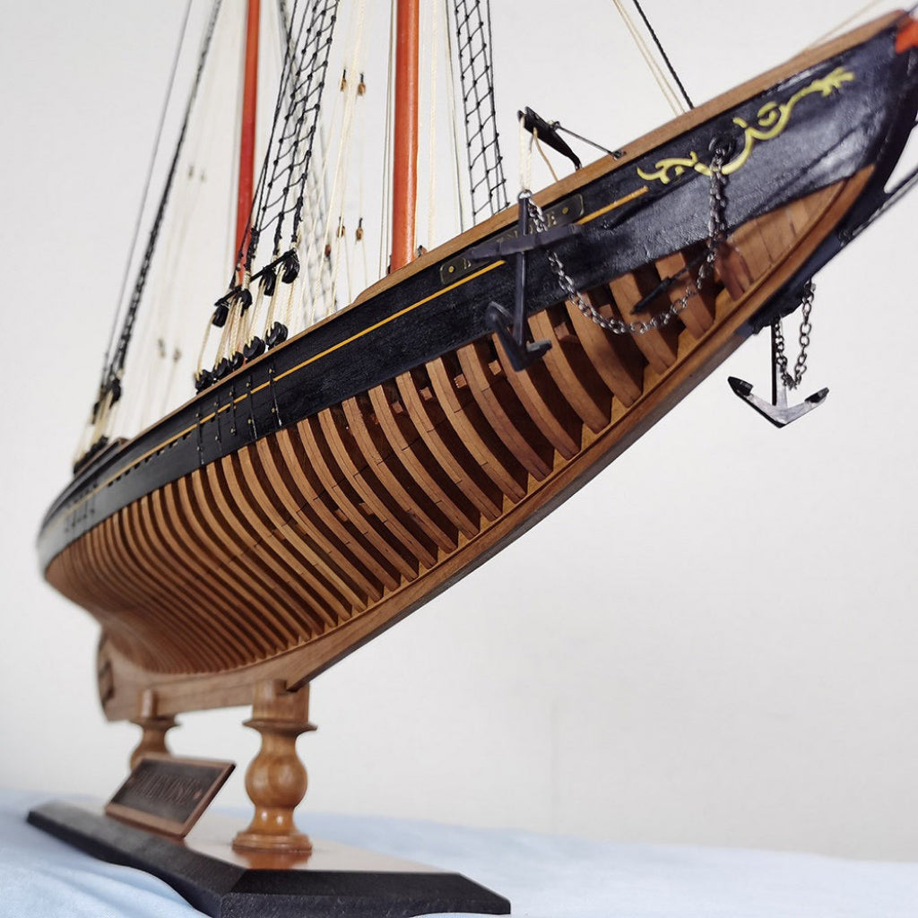 Close-up of Bluenose wooden ship model bow detail showing black painted hull gold scroll carving anchor chain and layered basswood plank framing