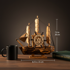Wooden sailboat model size comparison — 8.3 in long × 7.9 in tall (21 cm × 20 cm), shown next to a hardcover book and coffee mug for scale