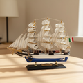 Italian Confection tall ship wooden model displayed on a light wood desk in a warm home setting, showing three-mast full-rigged white sails, blue-and-white striped hull, Italian flag, and brass Confection nameplate on black display base