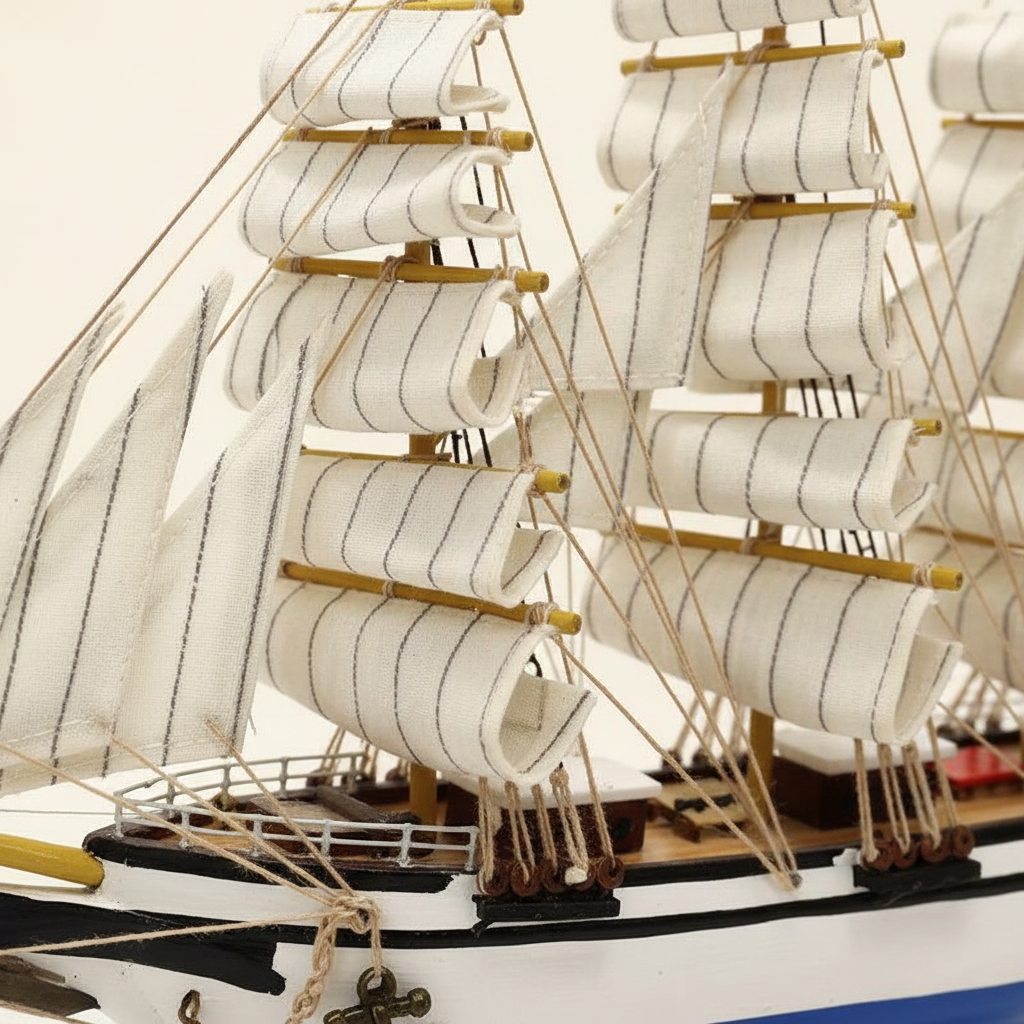 Close-up detail of Italian Confection tall ship wooden model showing white square-rigged sail texture, bamboo yard arms, rope rigging knots, deck railing structure, and blue-and-white hull planking craftsmanship