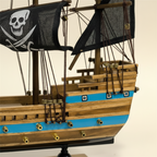 Modello in legno di nave pirata, dettaglio ravvicinato, con tre alberi, vele nere con teschio, scafo a righe blu e base nera
