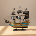 Modello in legno di nave pirata esposto su una scrivania in legno, con tre alberi, vele nere con teschio, scafo a righe blu e base nera