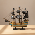 Modello in legno di nave pirata esposto su una scrivania in legno, con tre alberi, vele nere con teschio, scafo a righe blu e base nera