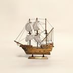 Side profile of Mayflower wooden ship model on cream background, showing complete three-mast silhouette with full white striped sails, rope rigging, warm walnut-tone planked hull with brass cannon port fittings, and wooden display base with gold Mayflower nameplate – 33 cm