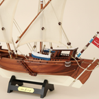 Close-up detail of Kuwait Dhow wooden ship model showing mahogany hull plank texture, white lateen sail fabric, rope rigging craftsmanship, and custom engraved nameplate on black display stand
