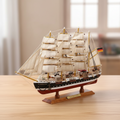 Handcrafted Passat four-masted barque wooden ship model displayed on a warm wooden desk in a home setting, black-and-white hull with red waterline, full white square sails, authentic rope rigging, German flag at stern, soft warm natural light