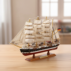Handcrafted Passat four-masted barque wooden ship model displayed on a warm wooden desk in a home setting, black-and-white hull with red waterline, full white square sails, authentic rope rigging, German flag at stern, soft warm natural light