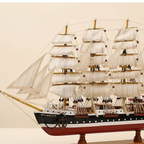 Close-up detail of Passat wooden ship model showing intricate rope rigging between masts, white square sail fabric texture, black-and-white hull planking with red waterline stripe, and custom engraved nameplate on wooden display base