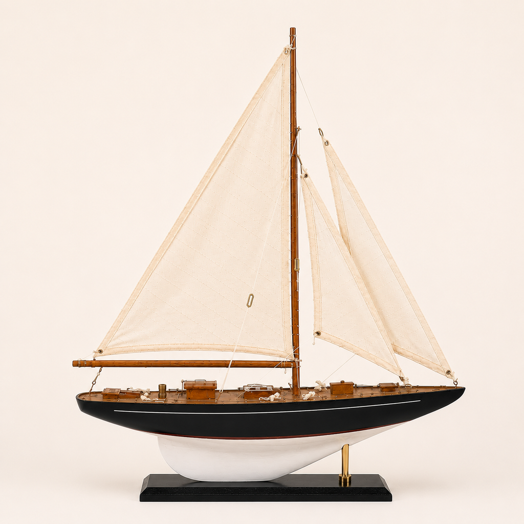 Vista lateral exacta de 90 grados de un modelo estadounidense de yate de vela de madera sobre fondo blanco crema, con silueta completa, un solo mástil, vela mayor y foque, casco oscuro con quilla blanca y base negra de exhibición