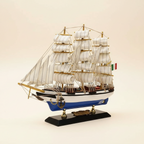  Rear 3/4 angle of Italian Confection tall ship wooden model on cream background, showing three-mast rigging structure, white square-rigged sails, Italian flag, blue-and-white hull stern section, and black display base with brass nameplate