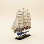  Front 3/4 angle of Italian Confection tall ship wooden model on cream background, showing three masts with full white square-rigged sails, rope rigging, blue-and-white hull, anchor at bow, and black display base with brass nameplate