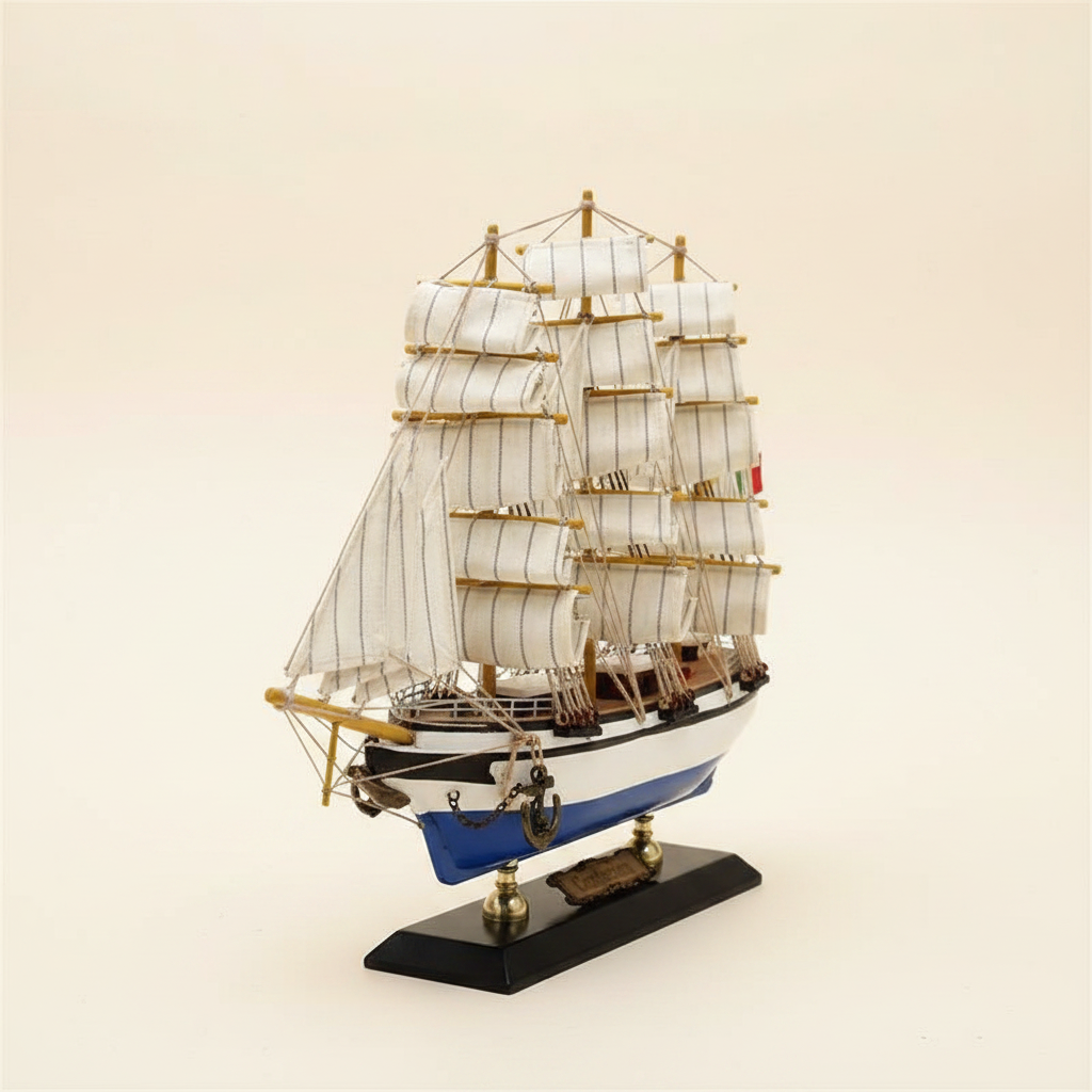  Front 3/4 angle of Italian Confection tall ship wooden model on cream background, showing three masts with full white square-rigged sails, rope rigging, blue-and-white hull, anchor at bow, and black display base with brass nameplate
