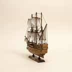 Rear 3/4 angle of Mayflower wooden ship model on cream background, showing high stern castle structure, three masts with white striped sails, rope rigging, warm walnut-tone planked hull, and wooden display base with gold Mayflower nameplate