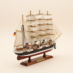 Handcrafted Passat four-masted barque wooden ship model rear three-quarter view showing stern, German flag, white square sails from behind, rope rigging detail, and black-and-white hull construction, cream white background