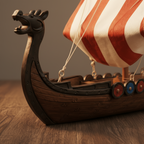 Close-up detail of Viking longship resin model showing carved dragon prow, painted red and blue shields, cord rigging, and wood-grain resin hull texture