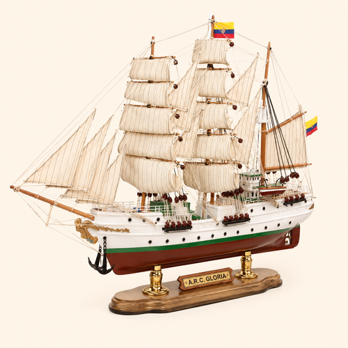 Front 45-degree view of the A.R.C. Gloria wooden sailing ship model on a cream background, showing the bow, layered cream sails, wooden masts, black anchor, gold bow ornament and Colombian flags.