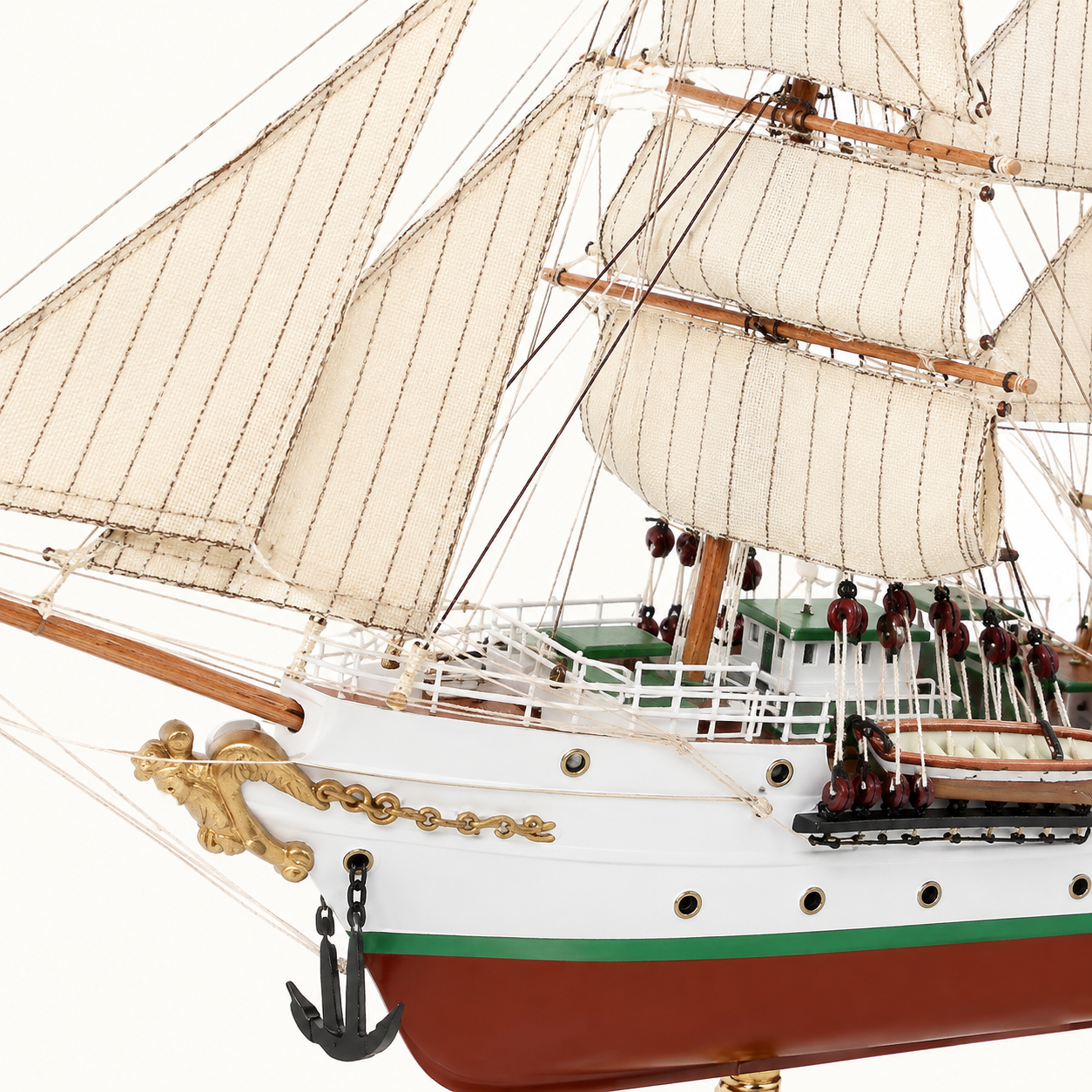 Close-up of the A.R.C. Gloria model ship showing textured cream sails, wooden spars, rope rigging, pulleys, white railings, green deck cabins, anchor chain and handcrafted hull details.