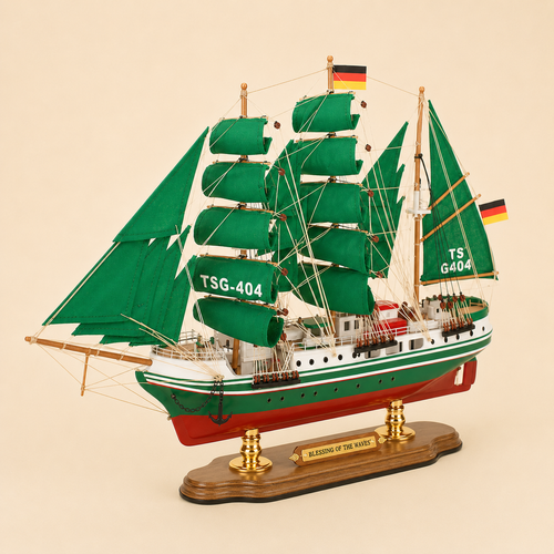 Front 45-degree view of the Alexander von Humboldt TSG-404 model ship on a cream background, showing the bow, layered green sails, wooden masts, black anchor, intricate rigging and German flags.