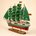 Rear 45-degree view of the Alexander von Humboldt wooden ship model showing the stern, rear deck, German flags, green fabric sails, detailed rigging and polished presentation base.