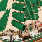 Close-up of the Alexander von Humboldt model ship showing textured green sails, wooden spars, rope rigging, pulleys, deck railings, cabins, anchor chains, portholes and handcrafted nautical details.