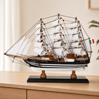 Amerigo Vespucci wooden tall ship model displayed on a light wood cabinet, featuring layered white sails, detailed dark rigging, black-and-white striped hull, Italian flag and black display base.