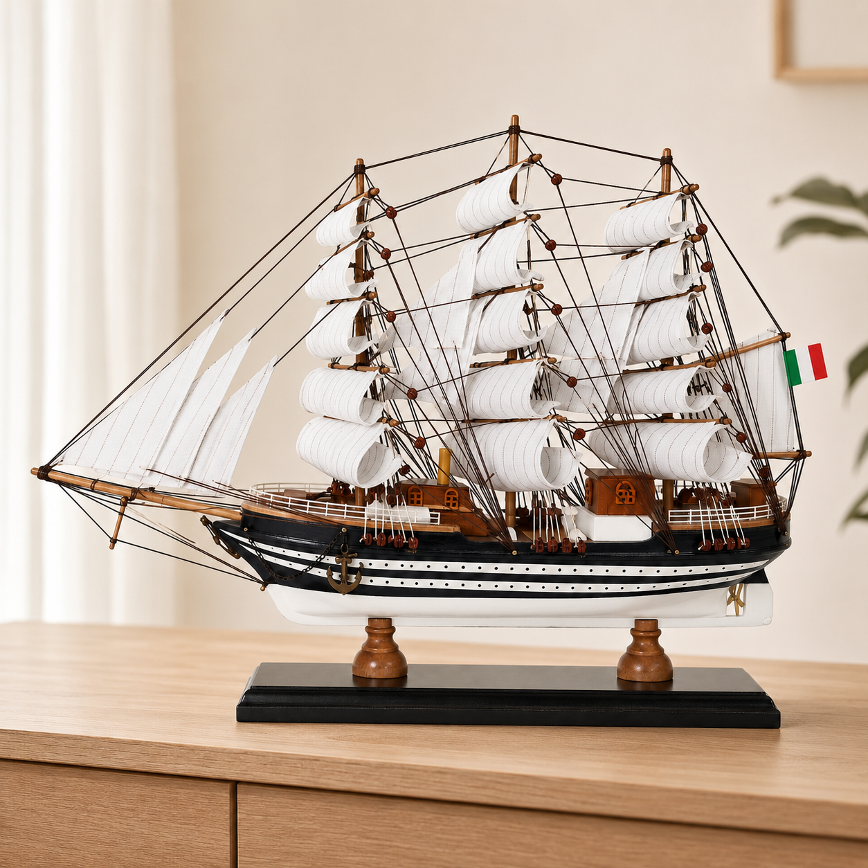 Amerigo Vespucci wooden tall ship model displayed on a light wood cabinet, featuring layered white sails, detailed dark rigging, black-and-white striped hull, Italian flag and black display base.