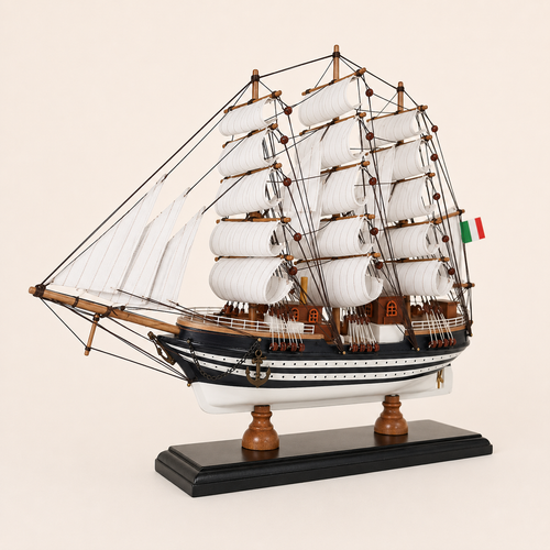 Front 45-degree view of the Amerigo Vespucci model ship on a cream background, showing the bow, white fabric sails, wooden masts, anchor, detailed rigging and Italian flag.