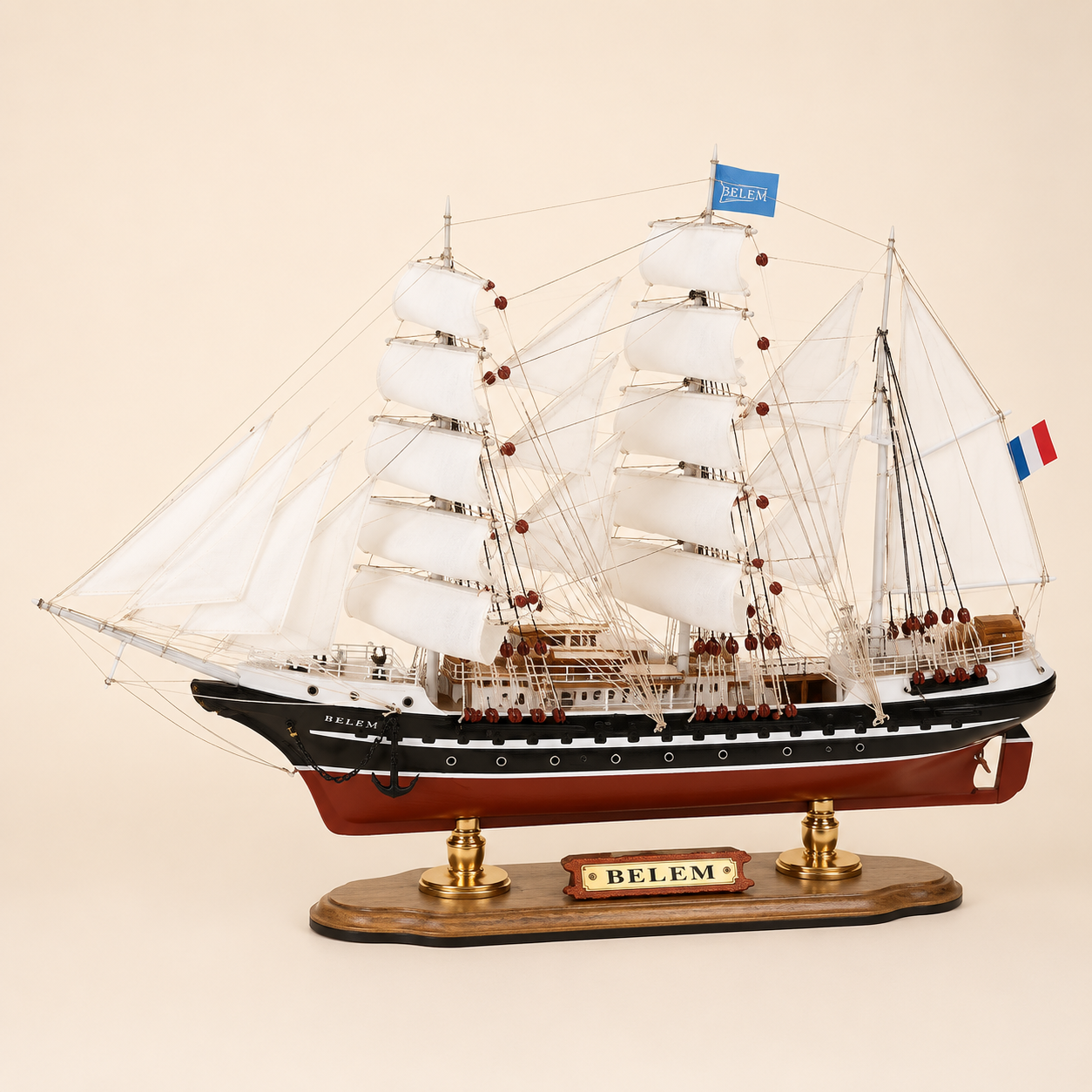 Side view of the Belem three-masted tall ship model featuring white sails, detailed rope rigging, black and white hull accents, red lower hull and wooden display stand.