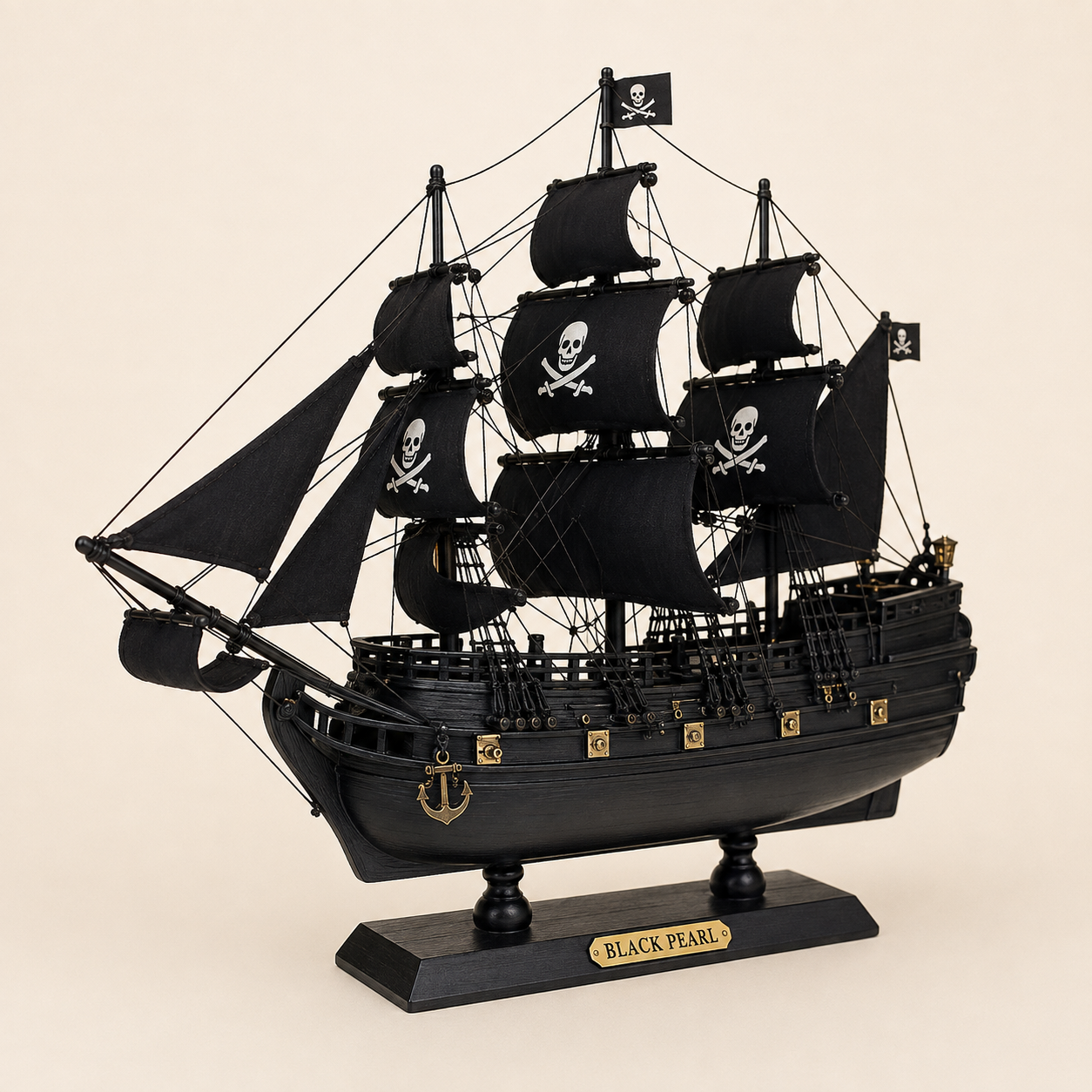 Front 45-degree view of the Black Pearl wooden pirate ship model on a cream background, showing the bow, layered black sails, pirate skull graphics, detailed rope rigging, black hull and gold nameplate.