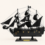 Side view of the Black Pearl three-masted pirate ship model featuring black fabric sails, skull-and-crossbones designs, intricate rigging, black wooden hull, gold decorative fittings and black display stand.