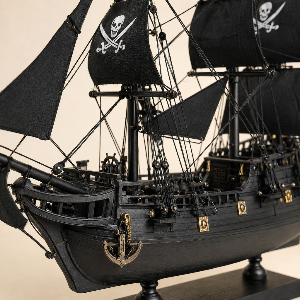 Close-up of the Black Pearl model ship showing textured black sails, skull-and-crossbones graphics, fine rope rigging, pulleys, deck railings, anchor, gold fittings and handcrafted hull details.
