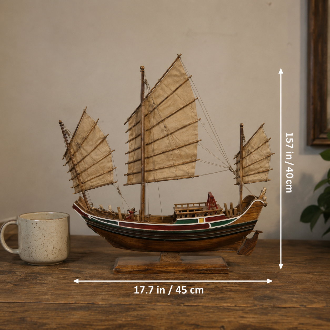 Model ship with sails on a wooden surface next to a mug, with dimensions indicated.