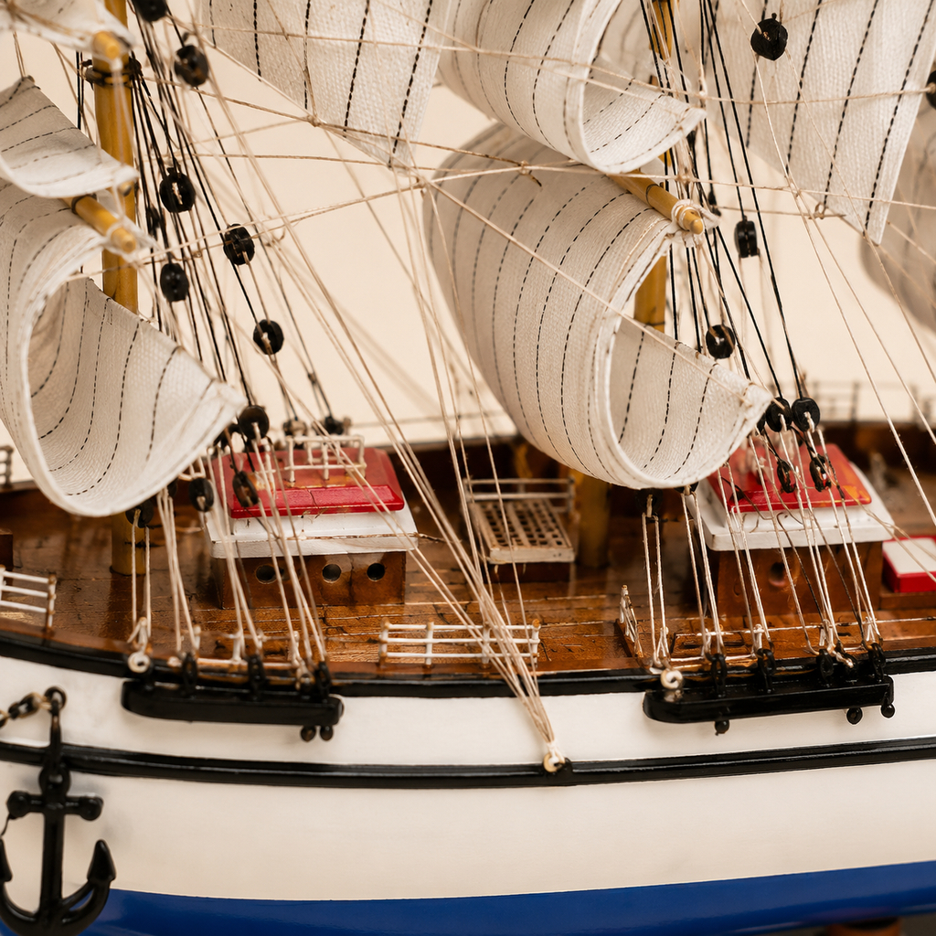 Close-up of the Italian Confection model ship showing textured cream sails, fine rope rigging, black pulleys, wooden deck, red-roofed cabins, white railings and handcrafted nautical details.