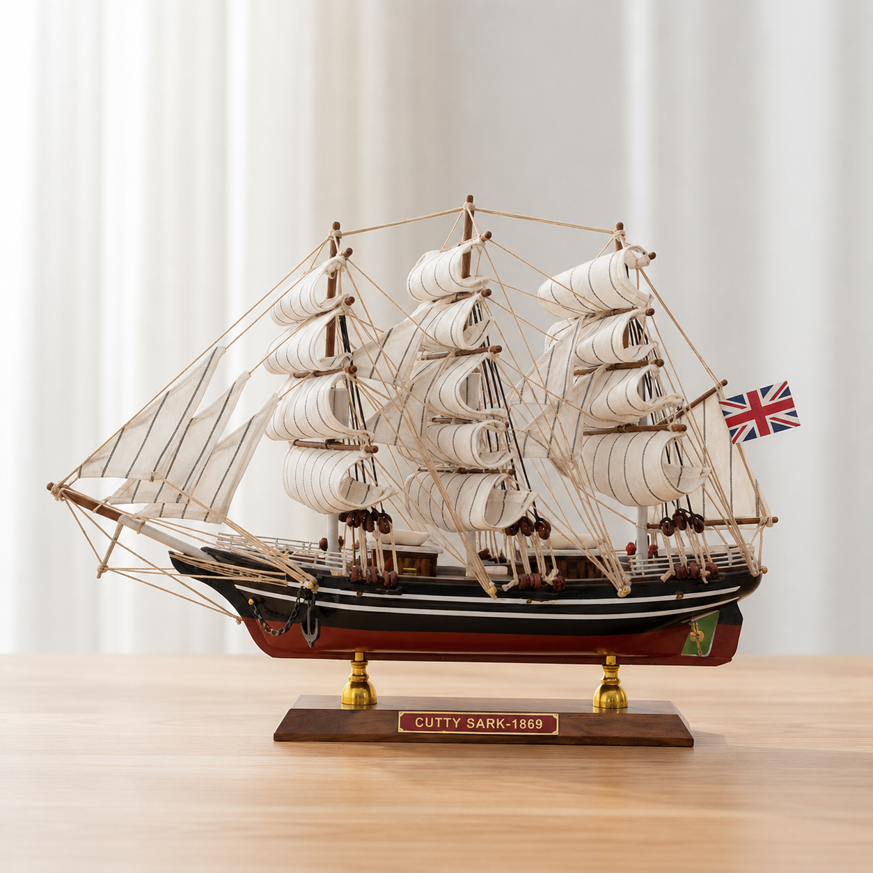 Cutty Sark 1869 model ship displayed on a light wooden table, featuring white fabric sails, detailed rope rigging, a black and red hull, British flag and wooden display stand.