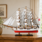 Large Danmark wooden tall ship model displayed on a wooden table, featuring white fabric sails, detailed black rigging, a white and red hull, Danish flag and black display base.