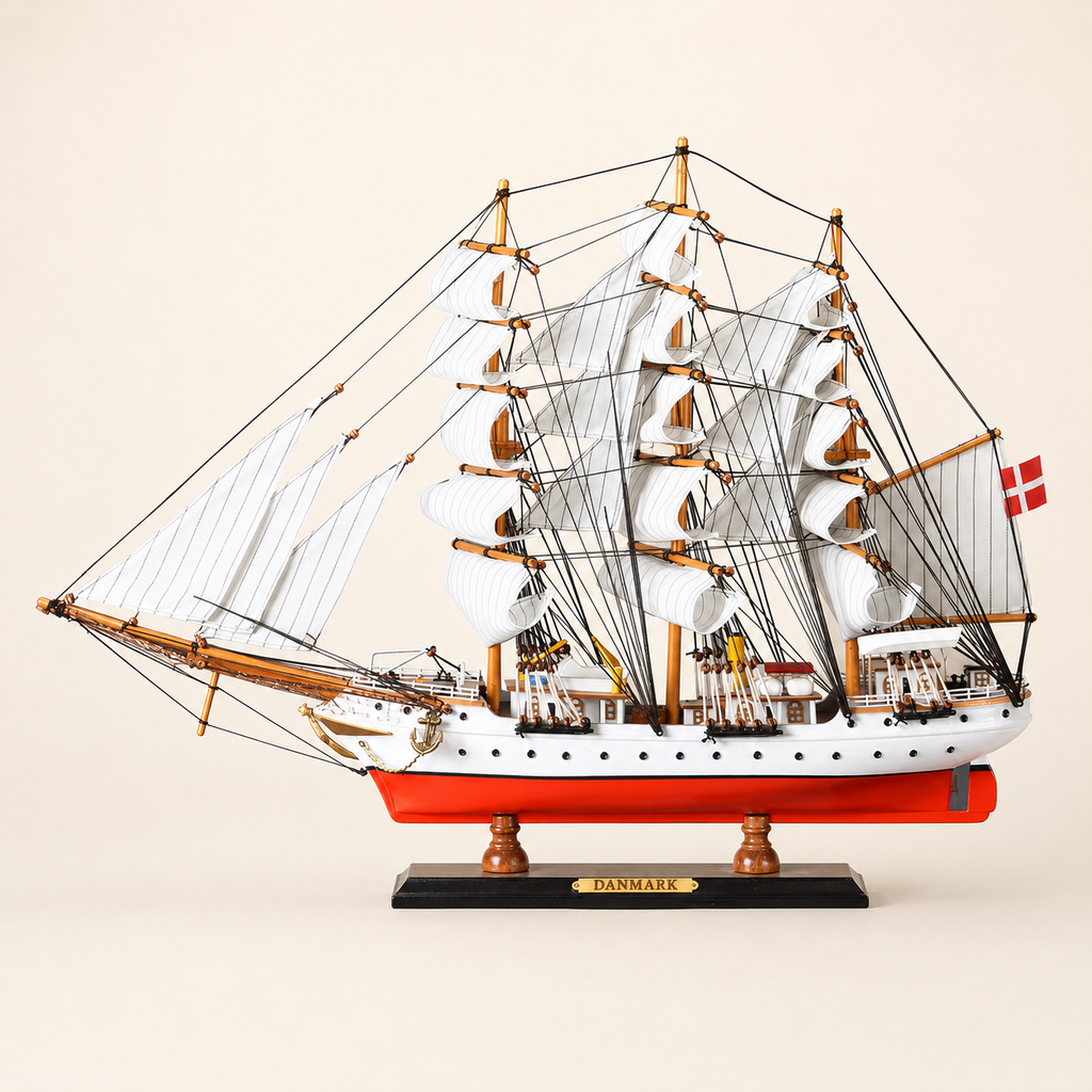 Side view of the Danmark three-masted tall ship model featuring white fabric sails, dense black rigging, a white hull, bright red lower hull and black presentation stand.