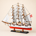 Rear 45-degree view of the Danmark model ship showing the stern, rear deck structures, Danish flag, layered sails, detailed rigging and black wooden display base.