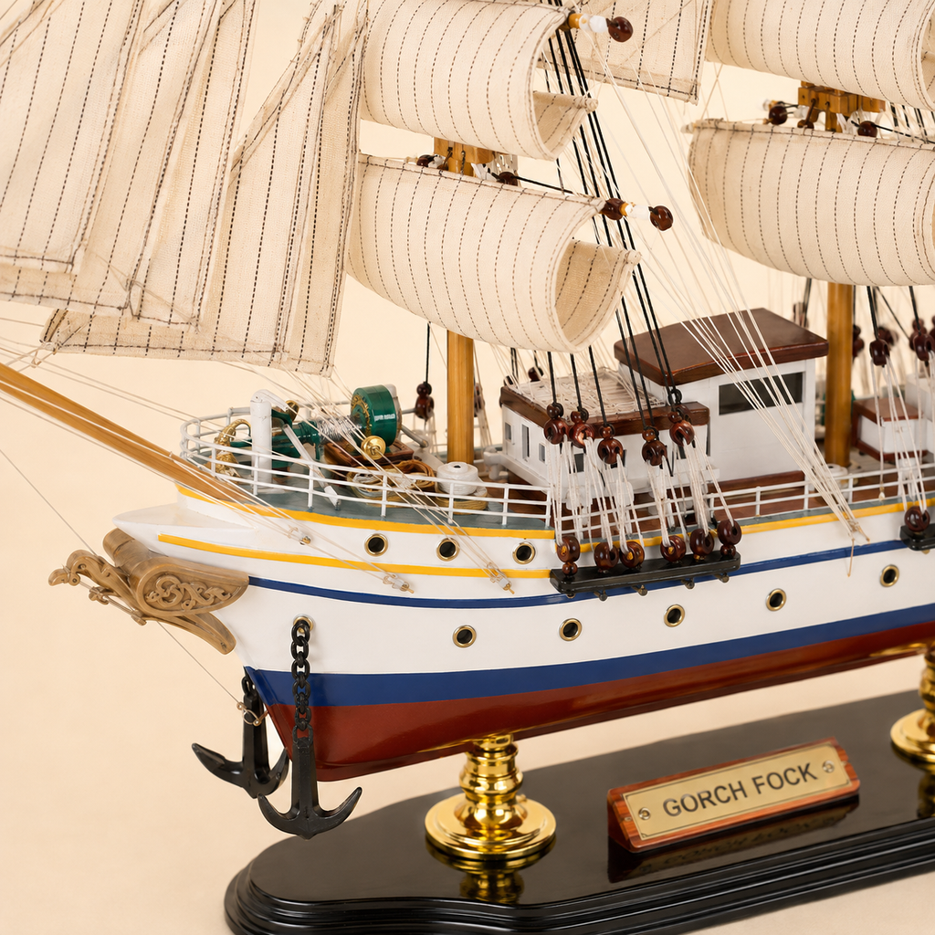 Close-up of the Gorch Fock model ship showing textured cream sails, rope rigging, wooden pulleys, deck cabins, railings, portholes, anchors and handcrafted nautical details.