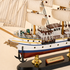 Close-up of the Gorch Fock model ship showing textured cream sails, rope rigging, wooden pulleys, deck cabins, railings, portholes, anchors and handcrafted nautical details.