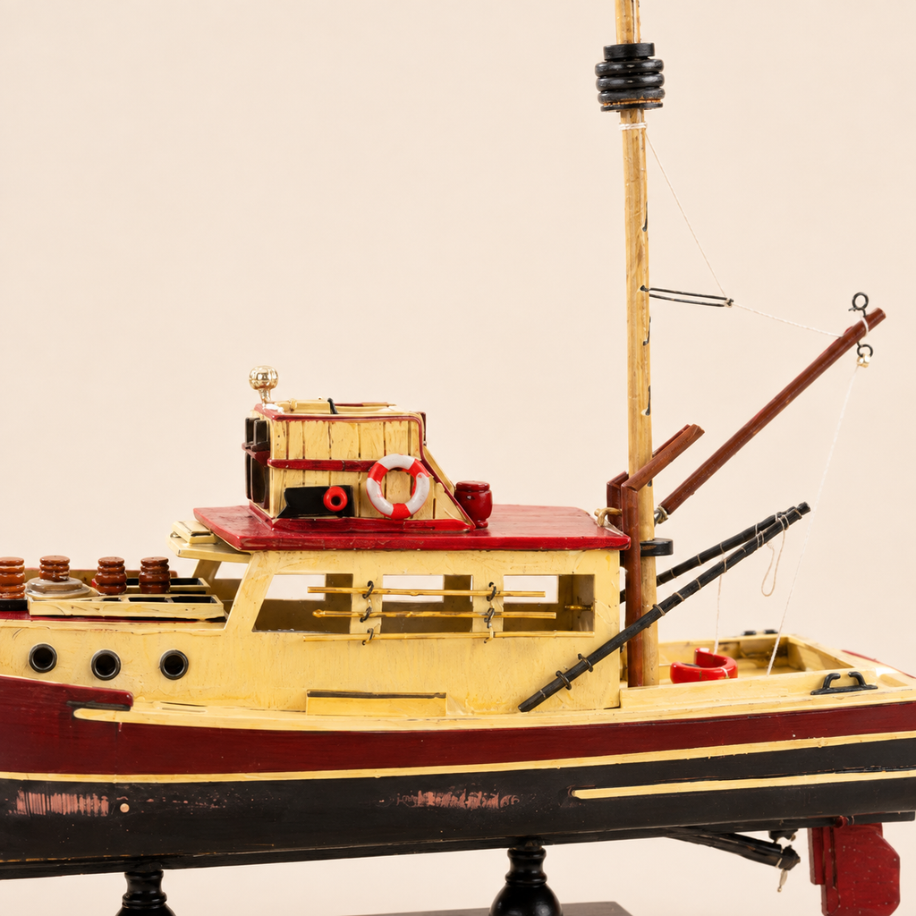 Close-up of the wooden fishing boat model showing the cream cabin, red roof, lifebuoy, portholes, mast fittings, crane arms, deck equipment and distressed painted hull details.