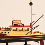 Close-up of the wooden fishing boat model showing the cream cabin, red roof, lifebuoy, portholes, mast fittings, crane arms, deck equipment and distressed painted hull details.