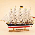 Side view of the Preussen five-masted tall ship model featuring multiple cream fabric sails, dense handcrafted rigging, black and white hull, red lower hull, deck structures and a wooden base with gold supports.