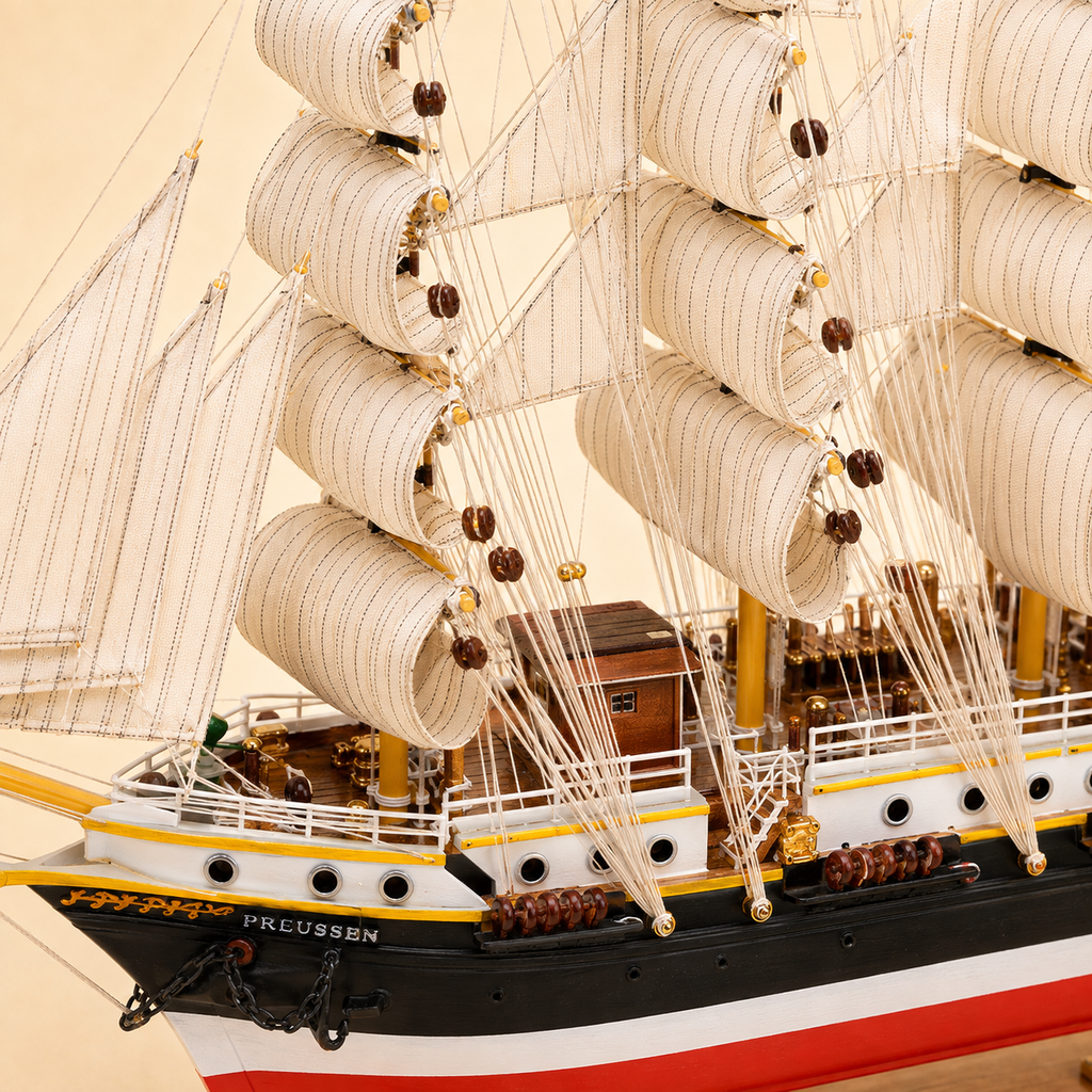 Close-up of the Preussen model ship showing textured cream sails, fine rope rigging, wooden pulleys, deck cabin, white railings, portholes, anchor chain and handcrafted black white and red hull details.