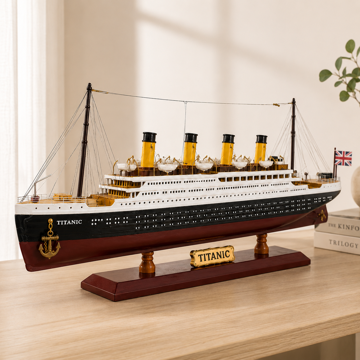 Large RMS Titanic model ship displayed on a light wood table in a bright modern interior, featuring four yellow funnels, detailed lifeboats, black and burgundy hull, Union Jack flag and wooden display stand.