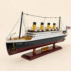 Front 45-degree view of the RMS Titanic model ship on a cream background, showing the bow, four yellow funnels, detailed deck structures, lifeboats, rigging and wooden display base.