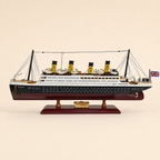 Side view of the RMS Titanic model ship featuring a black and white hull, burgundy lower hull, four yellow funnels, rows of portholes, lifeboats, rigging and Union Jack flag.