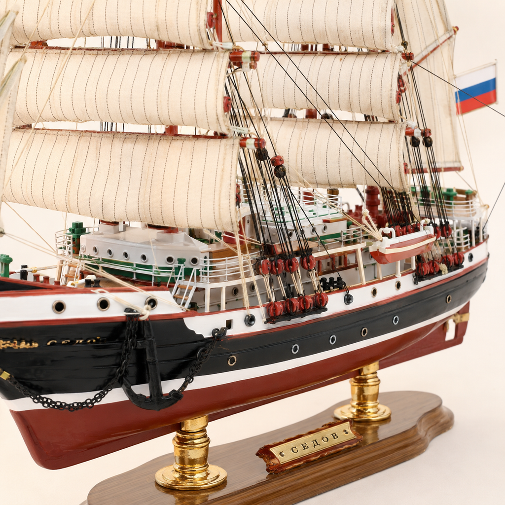 Close-up of the Sedov model ship showing textured cream sails, black and white rigging, red pulleys, deck railings, lifeboats, portholes, anchor chain and handcrafted hull details.