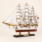 Front 45-degree view of the Sørlandet wooden ship model on a cream background, showing the bow, layered white sails, orange-brown masts, intricate rigging and Norwegian flag.