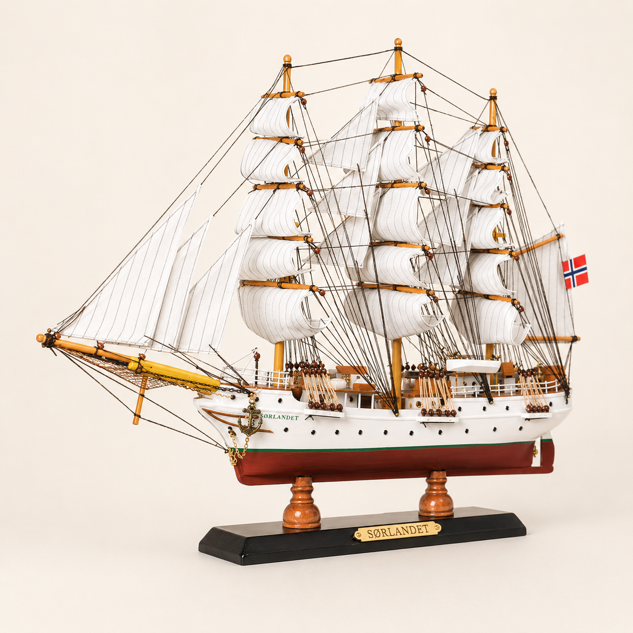 Front 45-degree view of the Sørlandet wooden ship model on a cream background, showing the bow, layered white sails, orange-brown masts, intricate rigging and Norwegian flag.