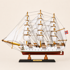 Side view of the Sørlandet three-masted tall ship model featuring white fabric sails, dense black rope rigging, white hull, green accent stripe, red lower hull and black stand.